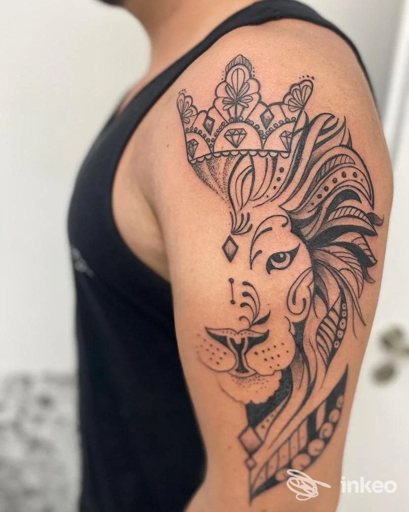 Tatuaggio a inchiostro nero raffigurante un leone ornamentale con corona sulla parte superiore del braccio e spalla, realizzato da Gino Tattoo - Art Bikers a Potenza.