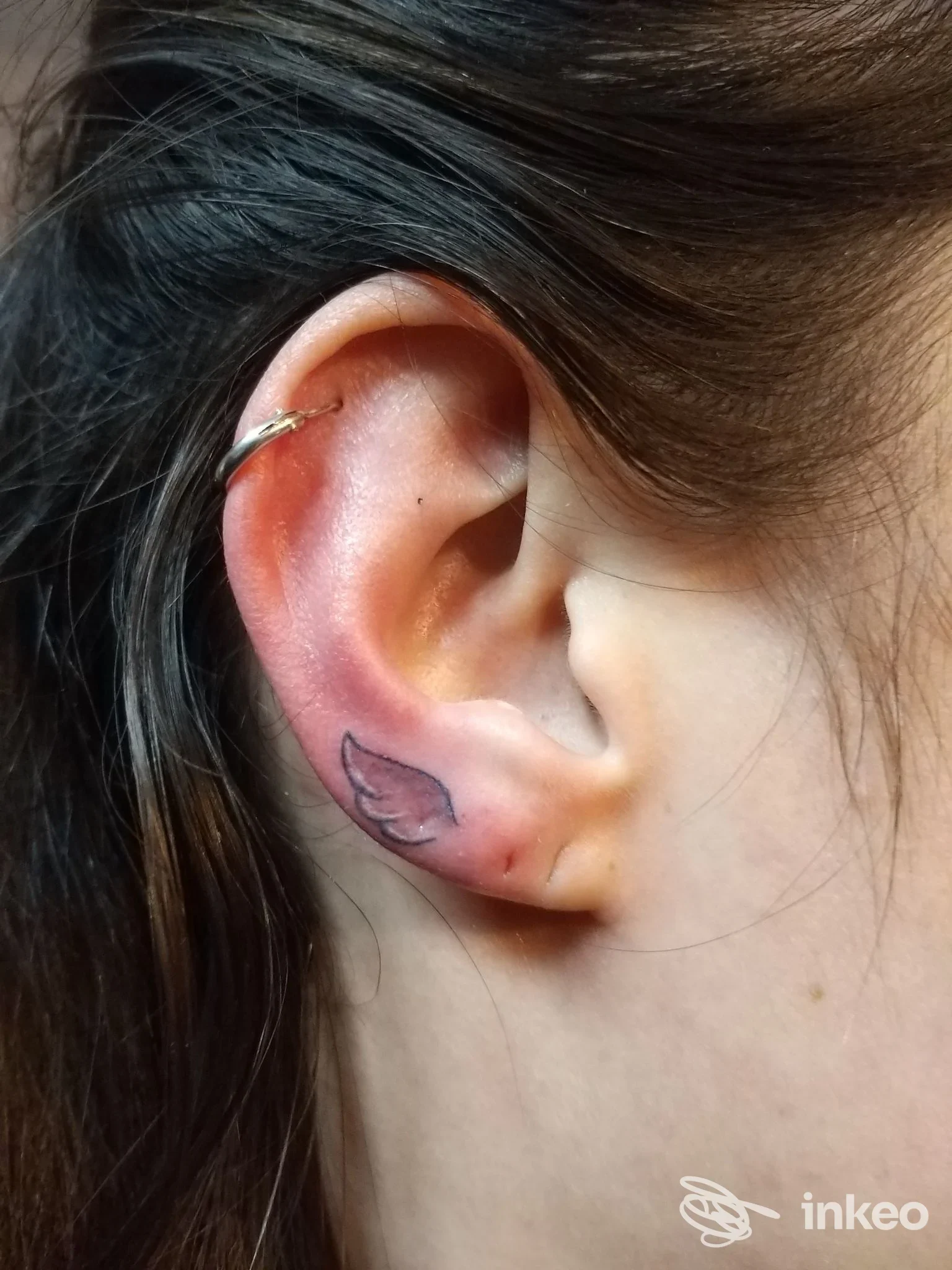 Foto ravvicinata di un piccolo tatuaggio a forma di ala sul lobo e un piercing all'elice, eseguiti da Nany Tattoo a Matera.