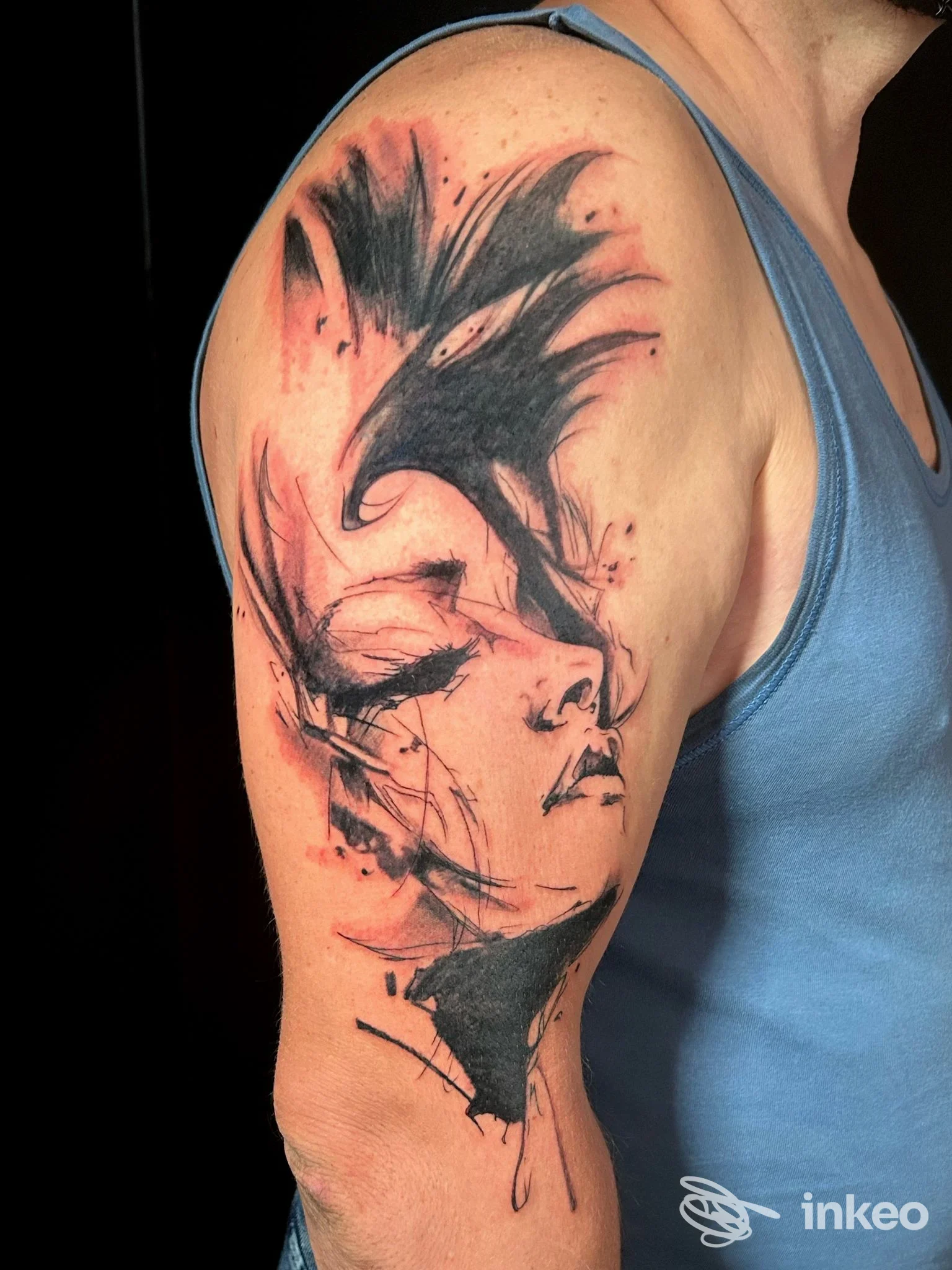 Foto del tatuaggio su spalla e braccio realizzato da Natalino Aghi e Inchiostro Studio Tattoo, Potenza: volto stilizzato in nero e rosso.