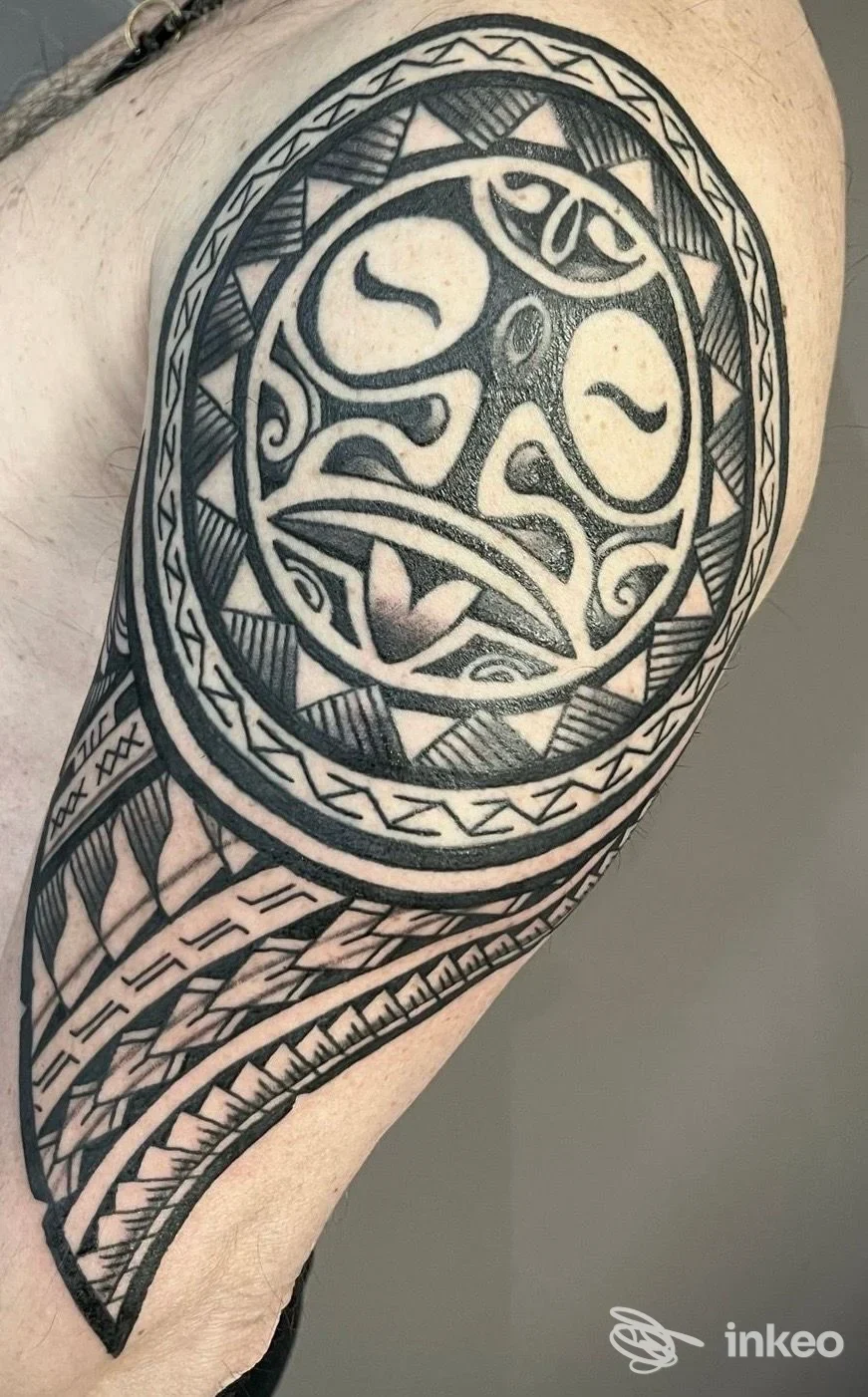 Tattoo circolare di stile tribale su braccio superiore, disegno in nero con cornice circolare e motivi geometrici, visibile pelle reale.