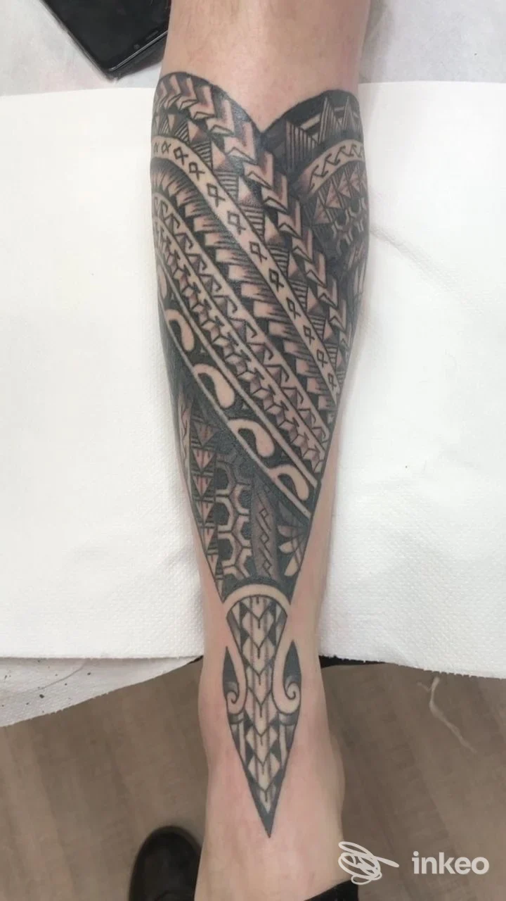Tattoo geometrico in nero su gamba, disegno tribale che va dalla tibia al polpaccio, su pelle reale.