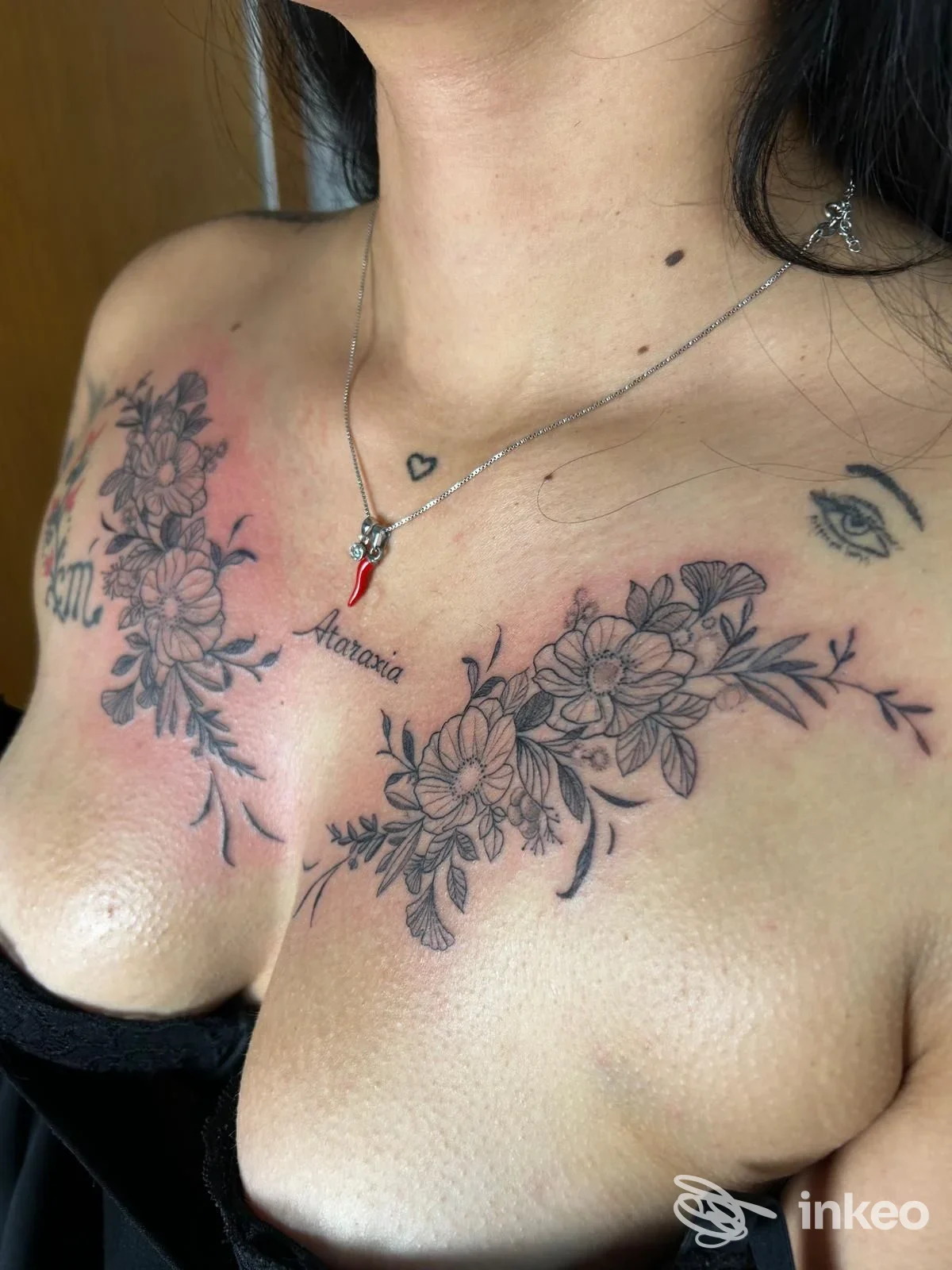 Primo piano di tatuaggio floreale sul petto realizzato da Sinkronia studio tattoo a Vietri di Potenza, mostra fiori e scritta centrale.