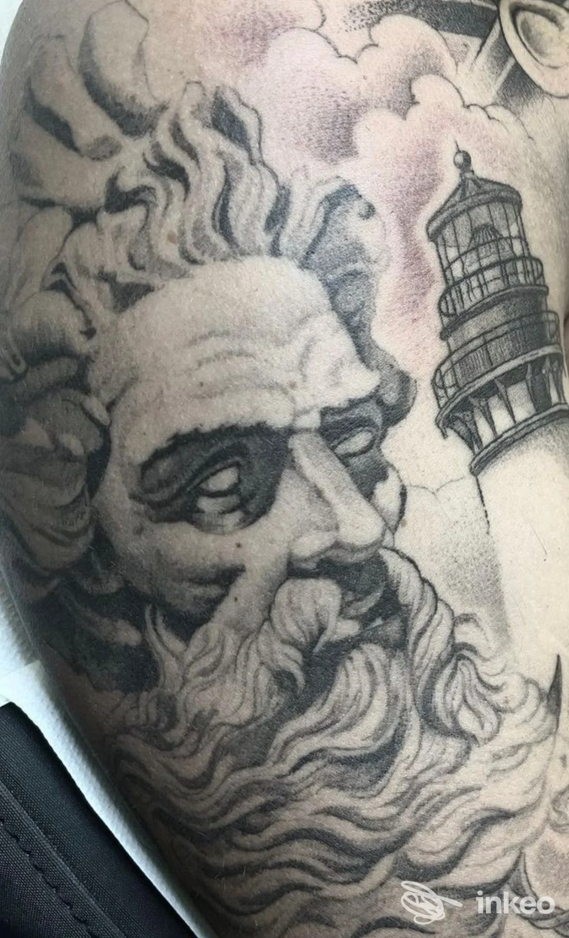 Tatuaggio in bianco e nero raffigurante un volto scultoreo e un faro sul braccio, Studio 69 Tattoo, Matera.