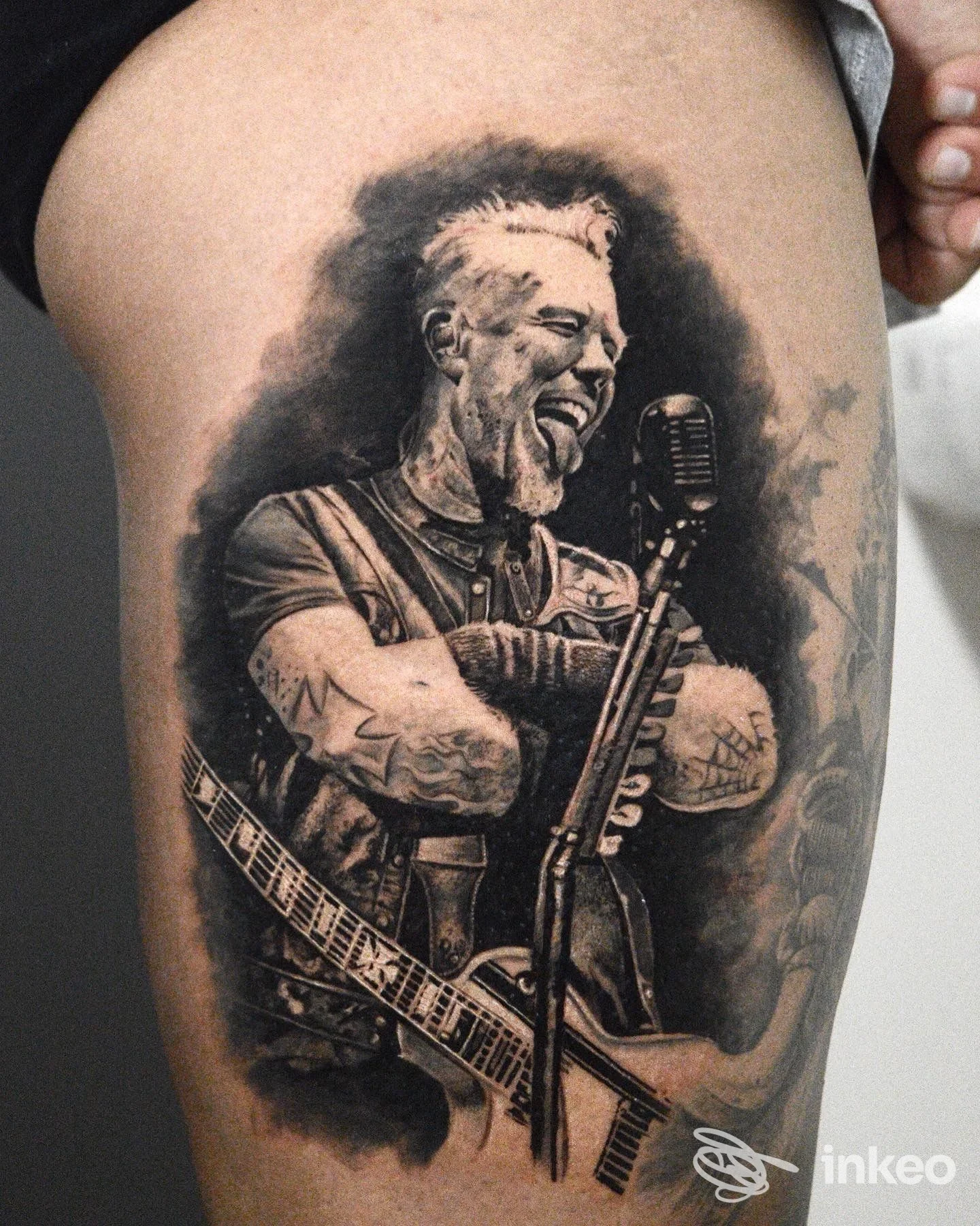 Tatuaggio realistico in bianco e nero su coscia raffigurante un musicista con microfono e chitarra, Tattoo Art Studio, Montescaglioso.