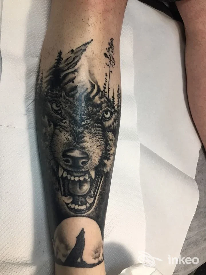Tatuaggio a inchiostro nero/grigio su avambraccio: muso di lupo ringhiante, alberi e luna. Tattoo Magic Skin, Potenza.