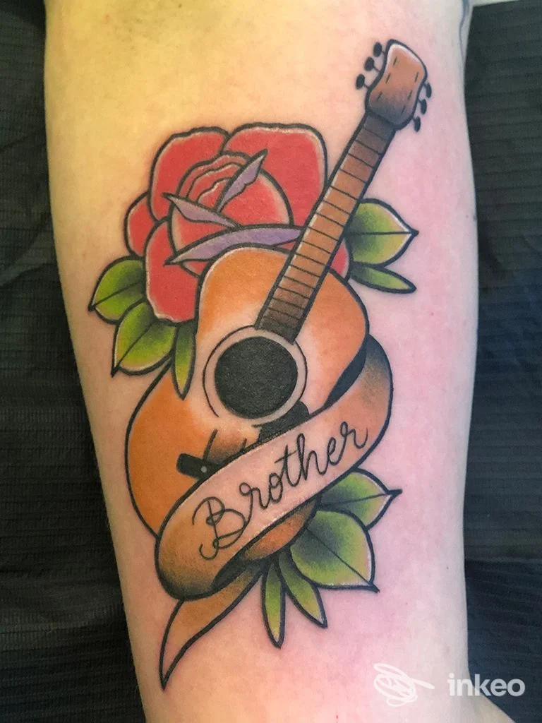 Tatuaggio tradizionale su antebraccio con chitarra, rosa e nastro scritto 'Brother' — Tintenfass Tattoo, Chiusa.