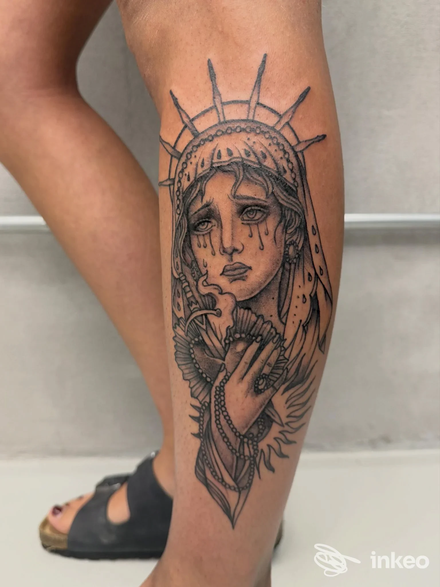 Tatuaggio in bianco e nero su polpaccio raffigurante un volto stilizzato che piange, foto fornita da kalashnikov art shop tattoo a Genova.