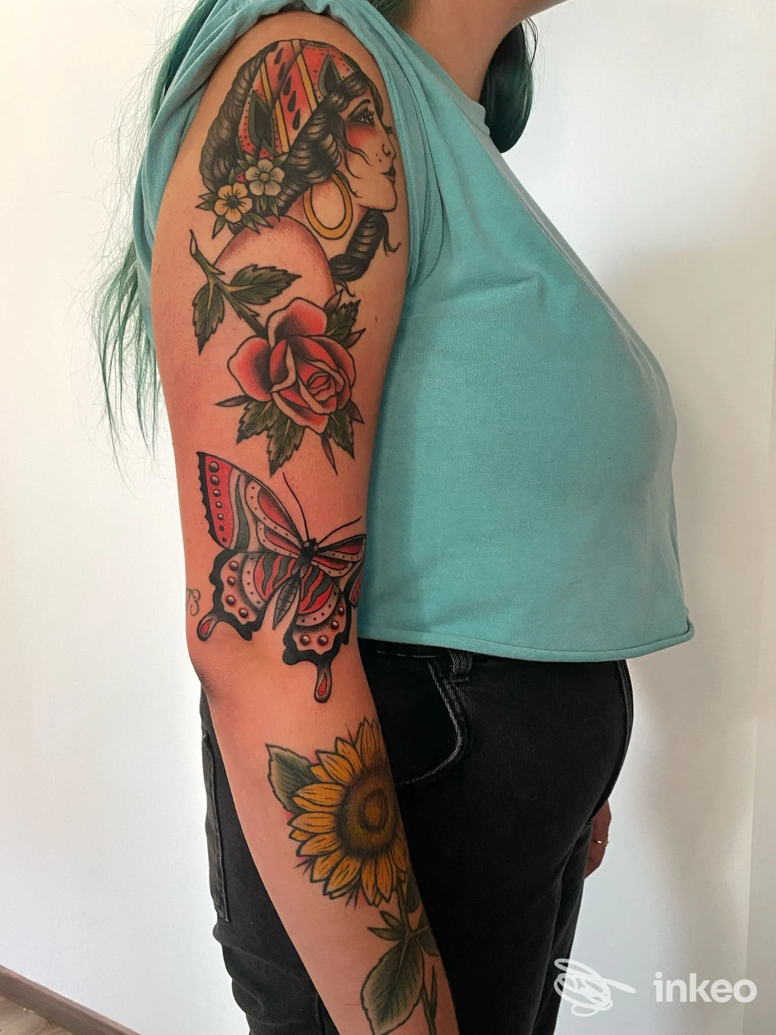 Braccio tatuato con più soggetti colorati (rosa, farfalla, girasole) — foto inviata dallo studio Sacred Bones Tattoo Bolzano, Bolzano.