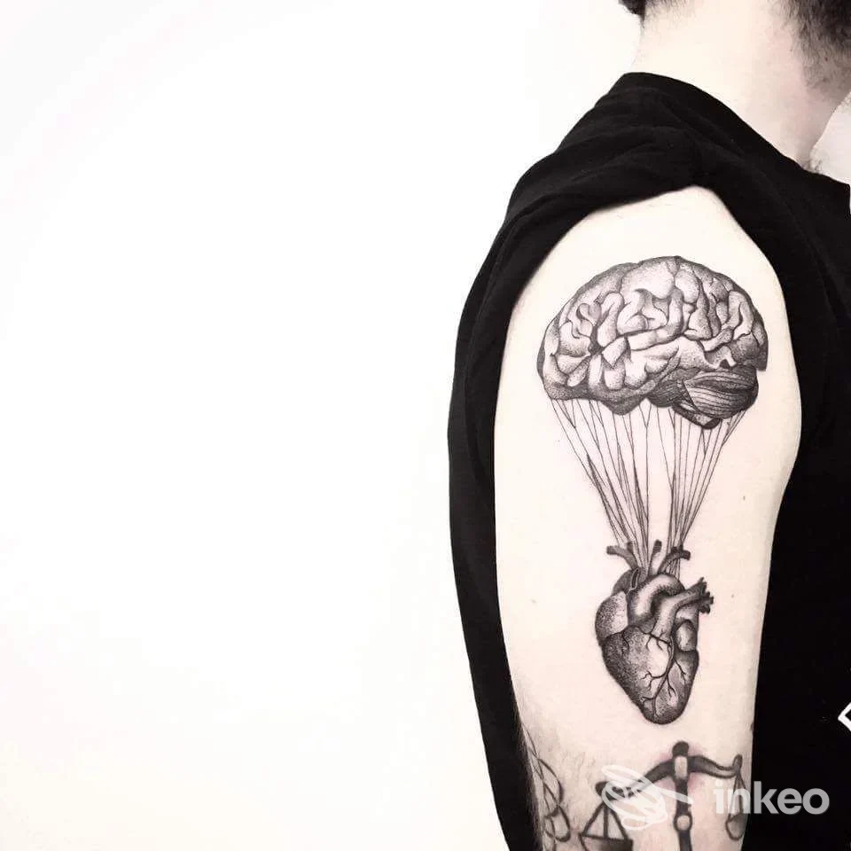 Tatuaggio realistico sul braccio superiore raffigurante un cervello sospeso sopra un cuore anatomico, immagine fornita da b/g tattoo, Livorno.