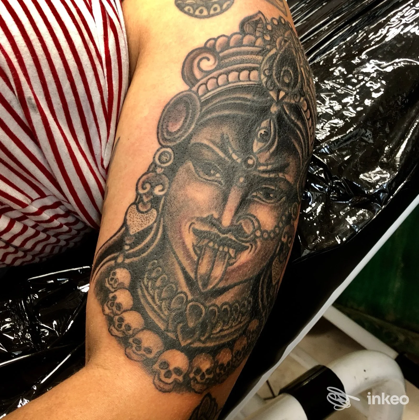Tatuaggio black & grey su avambraccio raffigurante volto mitologico con collana di teschi. Awake Tattoo, Prato.