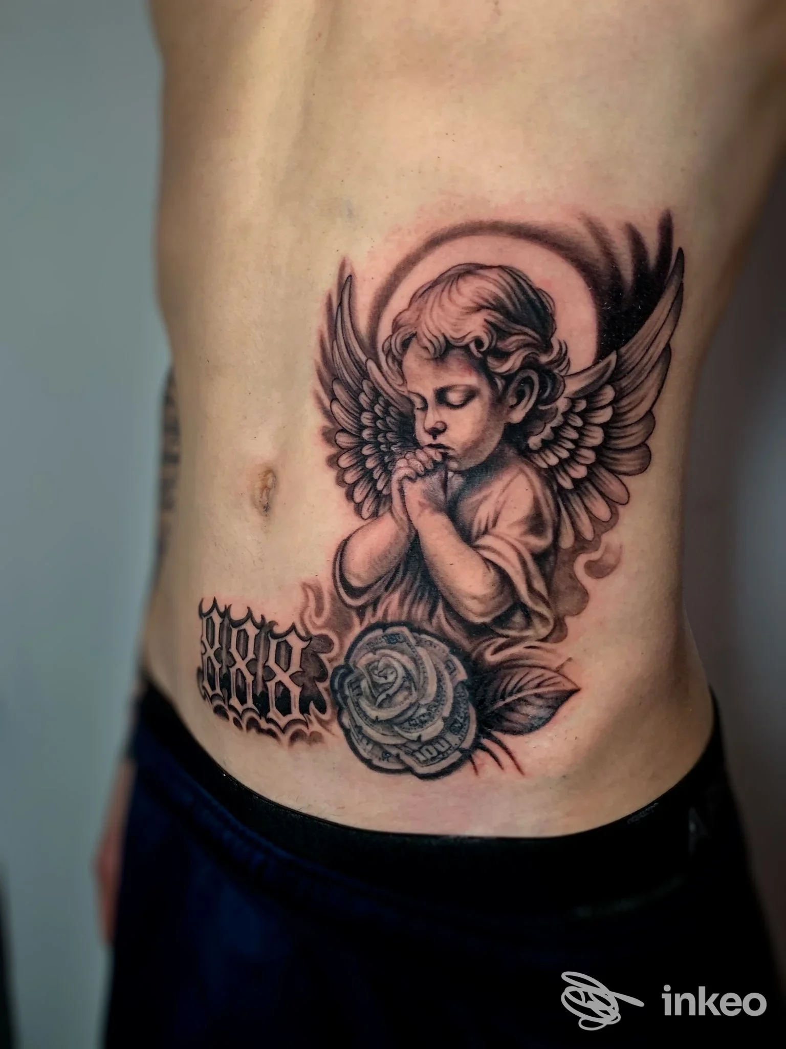 Tatuaggio realistico a inchiostro nero/grigio di un angelo con rosa e lettering, foto fornita da draive tattoo studio a Porto Viro.