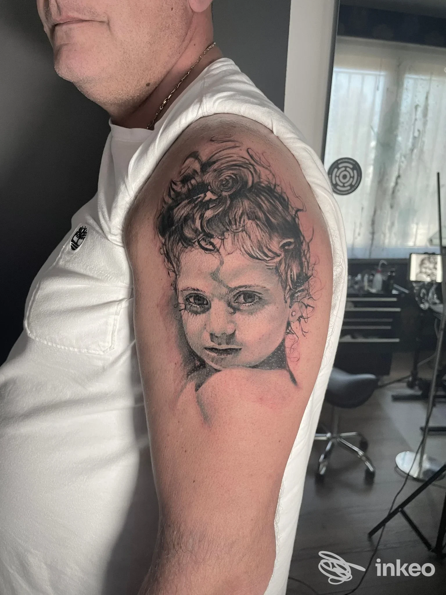 Tatuaggio realistico in bianco e nero del volto di un bambino sulla spalla, foto condivisa dallo studio ART World • Studio Tatuaggi, Po' Bandino.