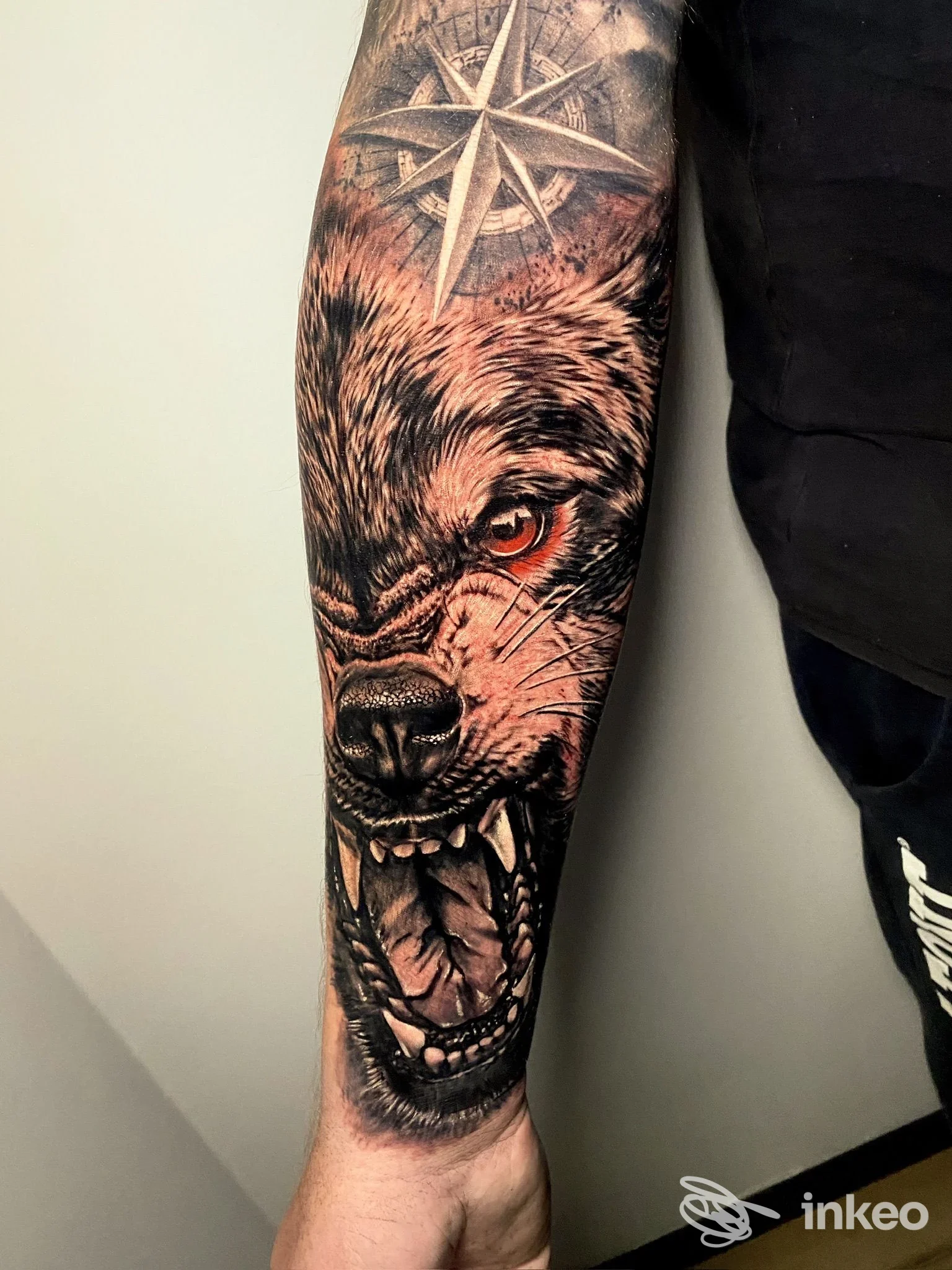 Tattoo realistico su avambraccio raffigurante un lupo che urla, con una stella a otto punte posizionata sopra la testa.