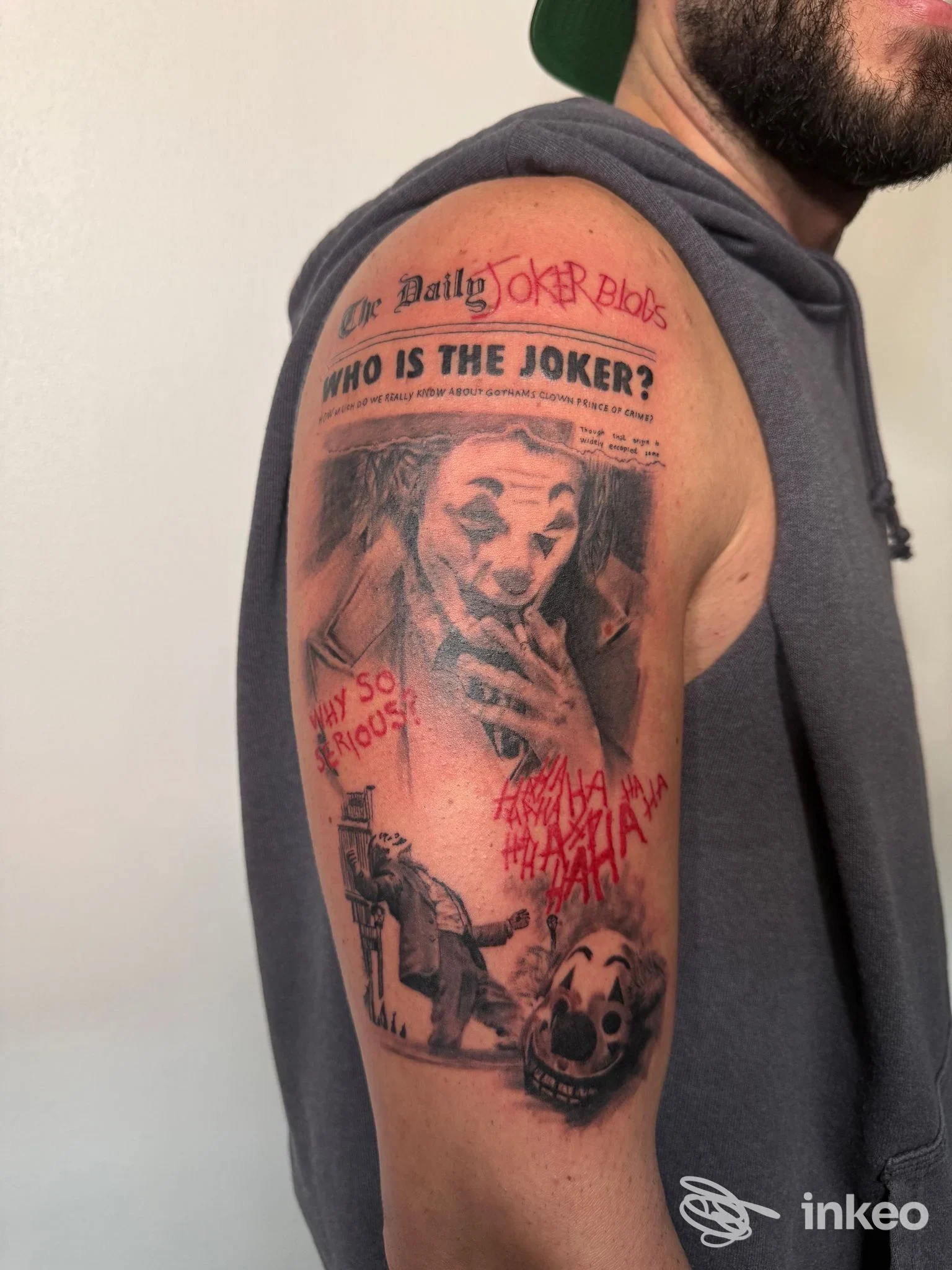 Tatuaggio Joker realistico in bianco e nero con accenti rossi sul bicipite, immagine fornita da Toky Tattoo Studio Bologna.