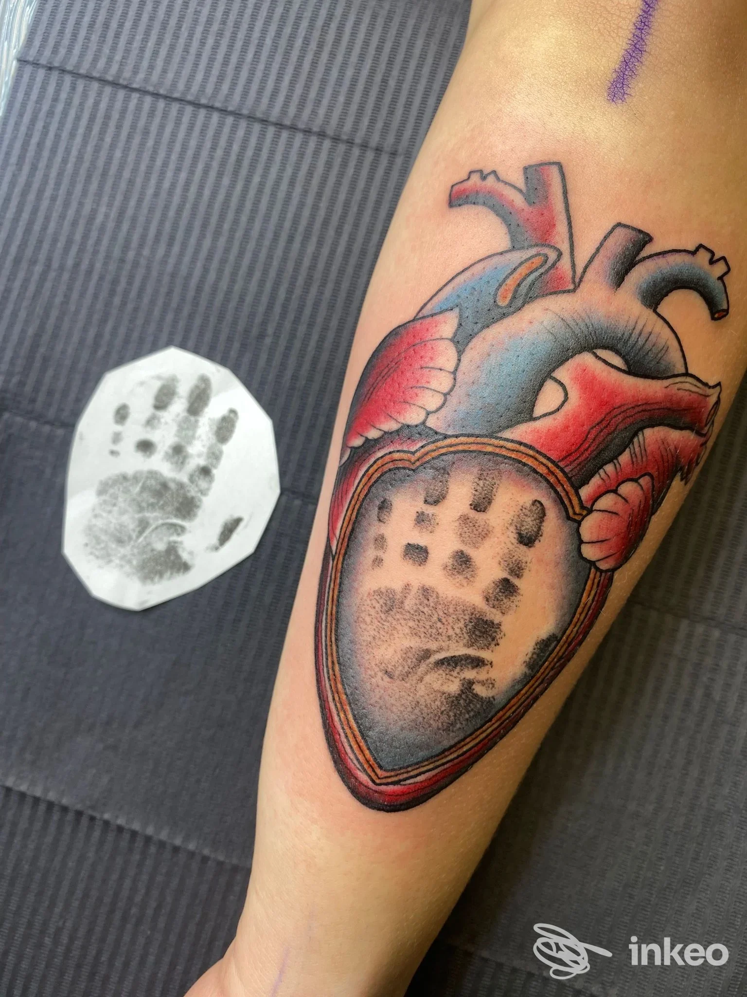 Primo piano di un tatuaggio su avambraccio: cuore anatomico colorato con impronta di mano nera, foto fornita da Cherry Tattoo & piercing, Imola.