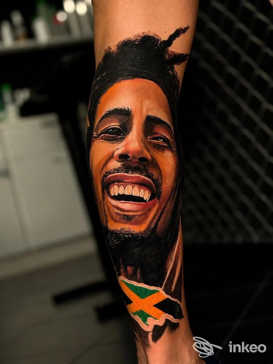 Tatuaggio ritratto realistico su avambraccio con bandiera giamaicana, realizzato da ZION INK Imola.