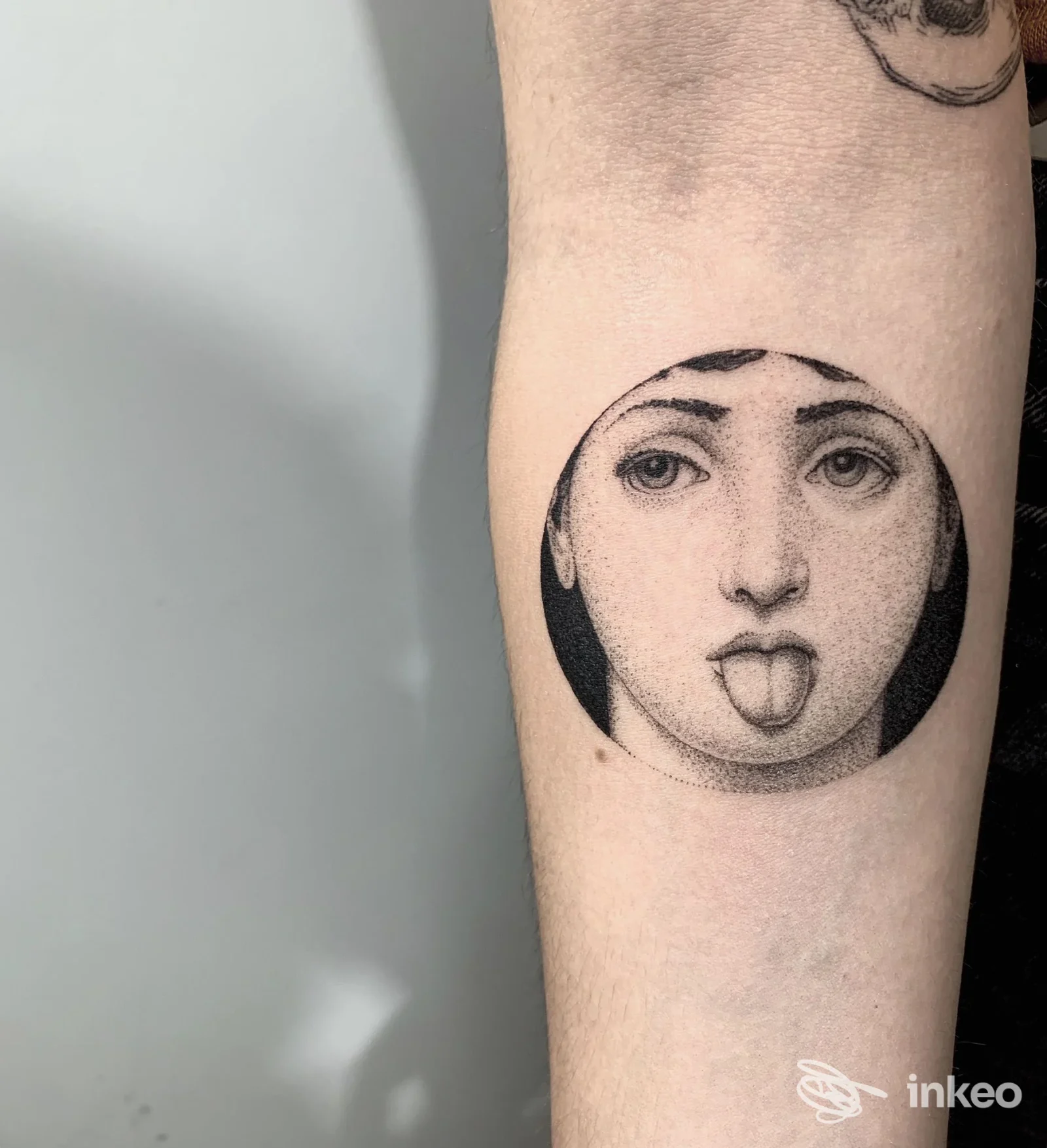 Tatuaggio circolare a puntinismo su avambraccio con volto che sporge la lingua, META tattoo lab, Bologna.