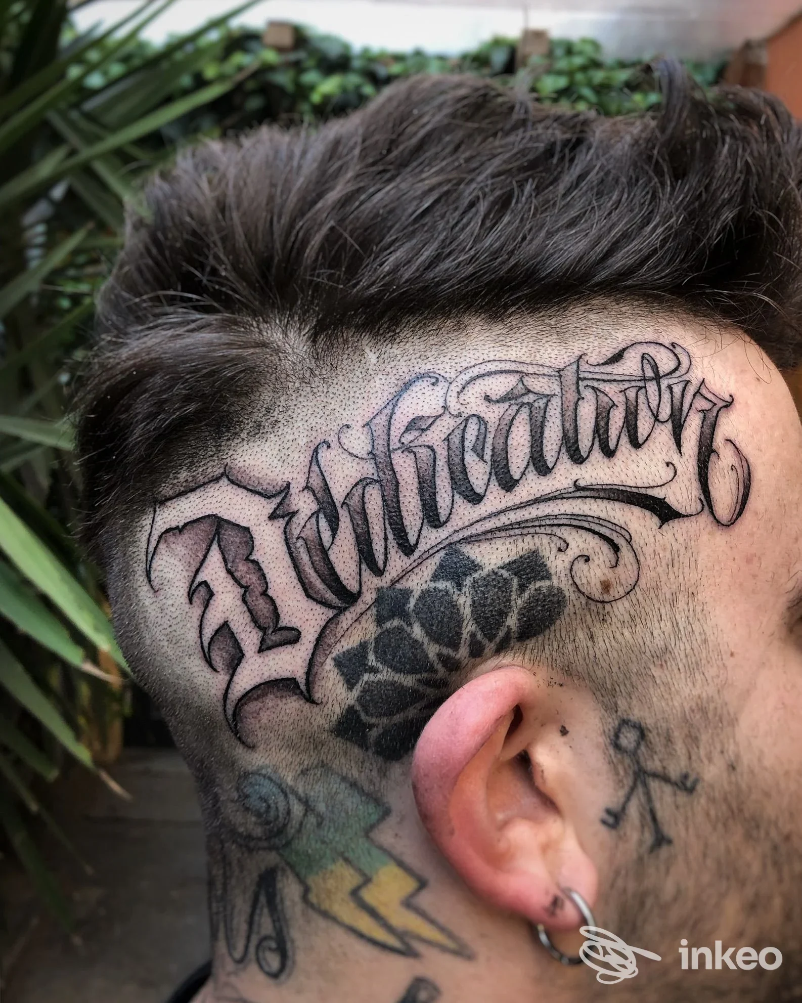 Tatuaggio lettering e decoro sul lato della testa, Dice Tattoo Shop a Bologna, vista laterale con piercing all'orecchio.