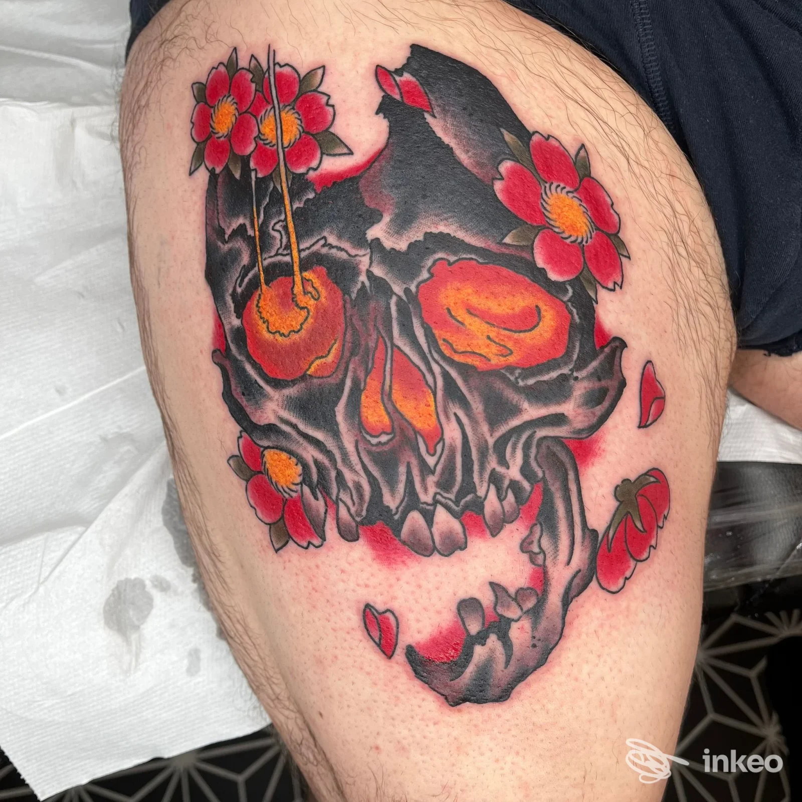 Tatuaggio grande su coscia con teschio nero e arancio e fiori rossi, foto fornita da Dice Tattoo Shop, Bologna.