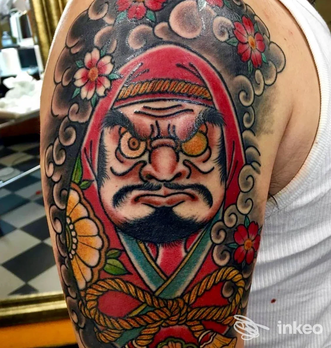 Tatuaggio a colori su braccio con figura Daruma, nuvole e fiori — Imperium Tattoo Gallery, Bologna.