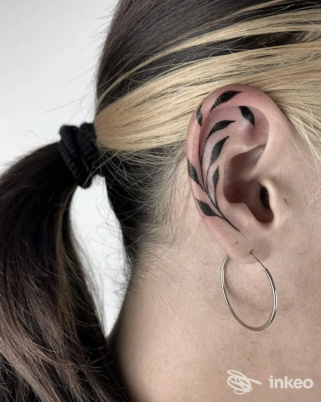 Primo piano di un tatuaggio nero a motivi fogliari sull'orecchio, scatto da Nero Tattooing a Bologna.