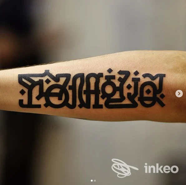 Tattoo visibile sull'avambraccio, disegno grafico in nero, stile decorativo, nessun volto o elemento esterno presente, immagine singola di una realizzazione corporea.