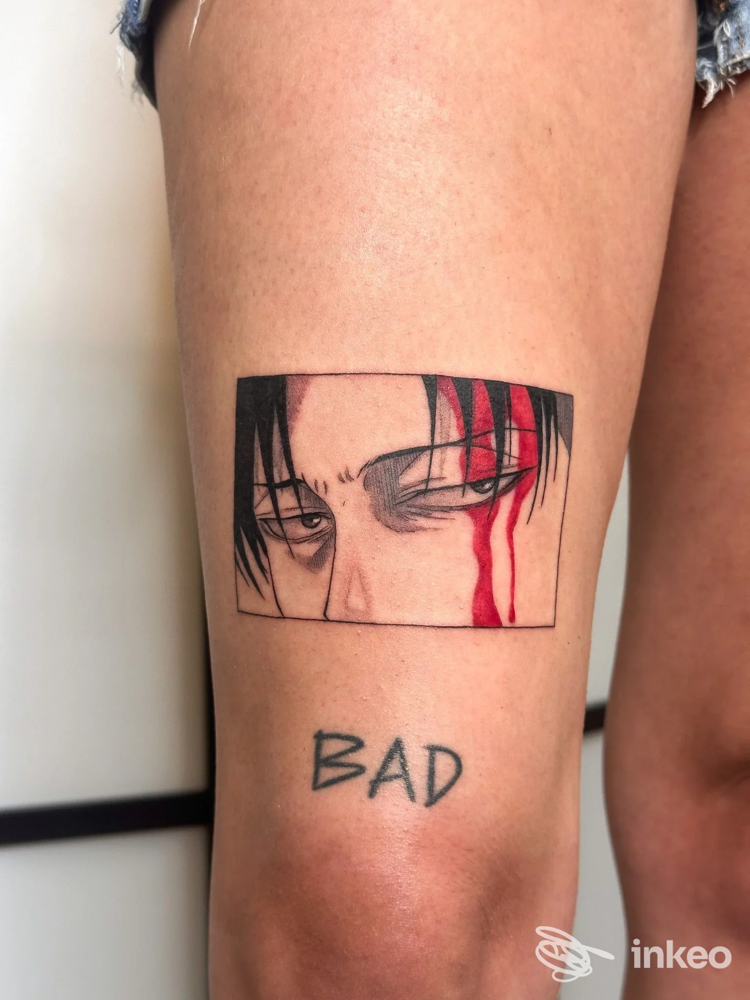 Primo piano su coscia di un tatuaggio a riquadro con occhi stilizzati e gocce rosse, con la scritta 'BAD' sotto; foto da Ink Rei Tattoo, Faenza.