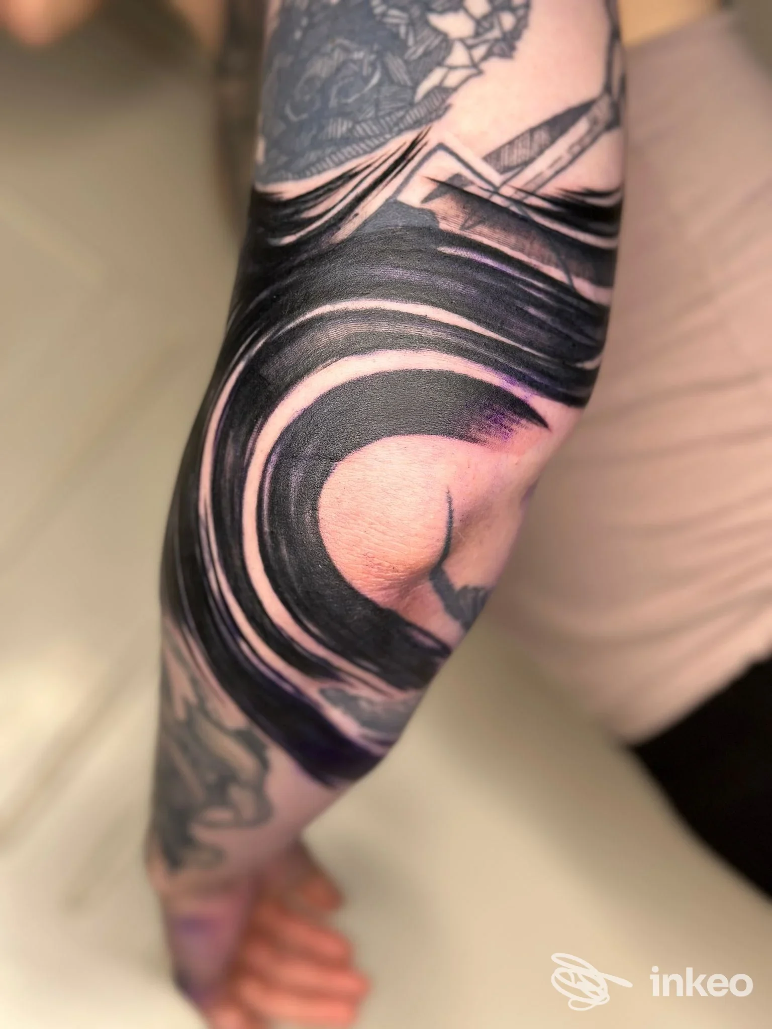 Primo piano dell'avambraccio con un grande tatuaggio nero e sfumature viola che avvolge il gomito, fotografia eseguita da Saint Ink Tattoo Studio, Bologna.
