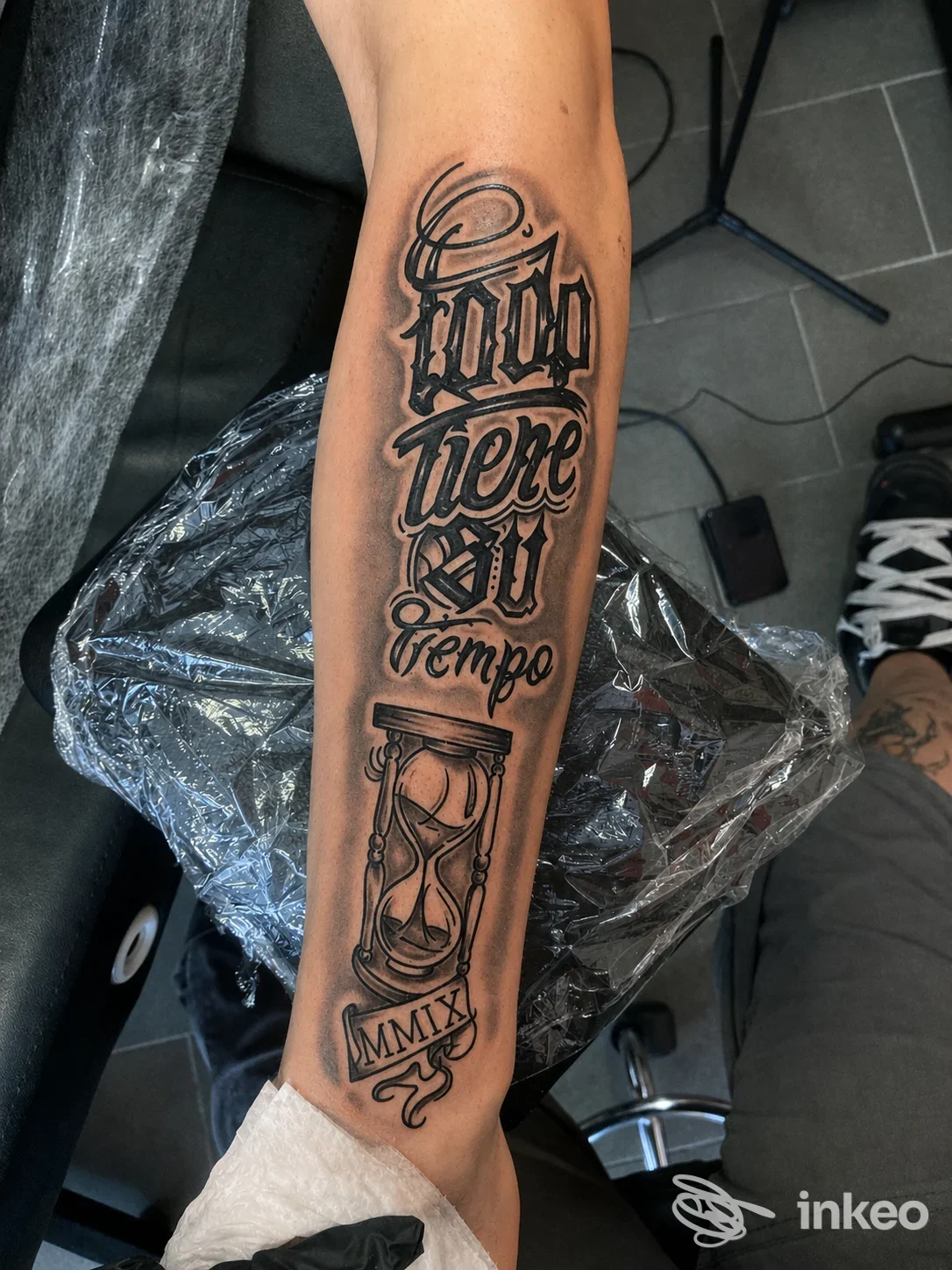 Tatuaggio in nero sull'avambraccio con lettering ornamentale e una clessidra, lavoro realizzato da TITANI TATTOO a Riolo Terme.