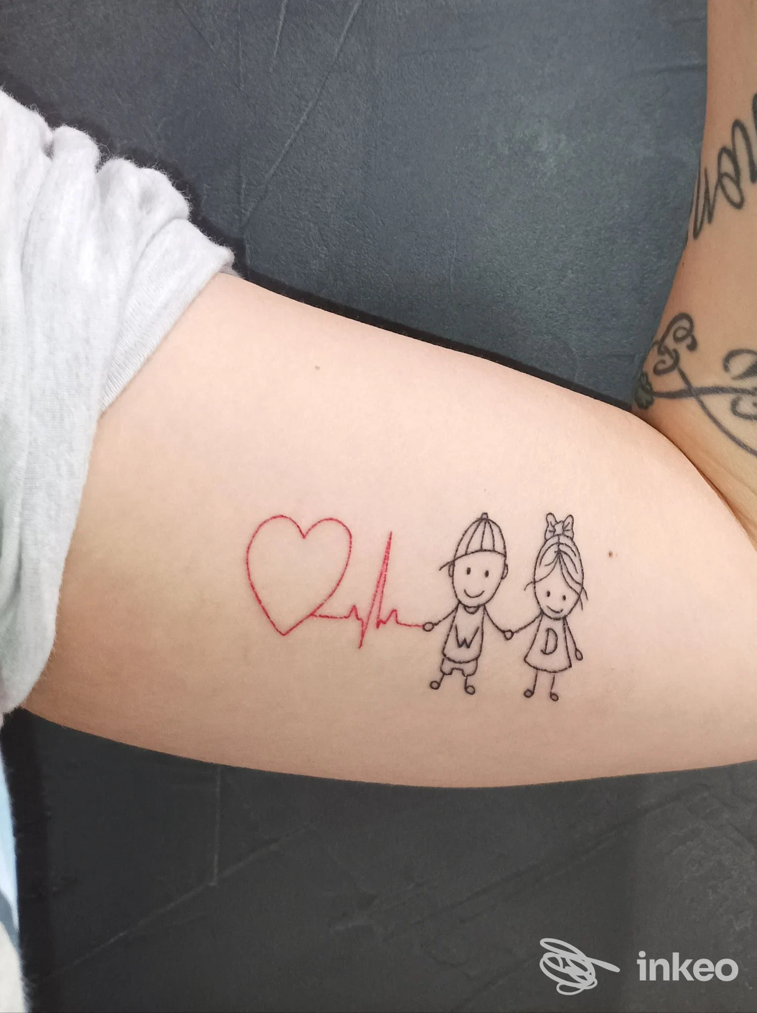 Tatuaggio sul bicipite con cuore rosso, tracciato cardiaco e due omini stilizzati, immagine fornita da Soul ink tattoo studio a Pollena Trocchia.