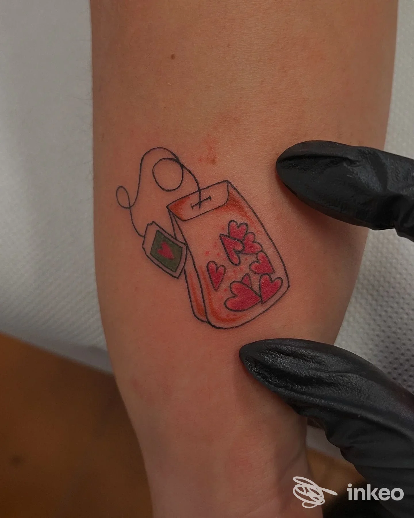 Piccolo tatuaggio colorato a forma di bustina di tè con cuori sull'avambraccio, fotografato nello studio BOTTEGANERA tattoos and more a Bologna.