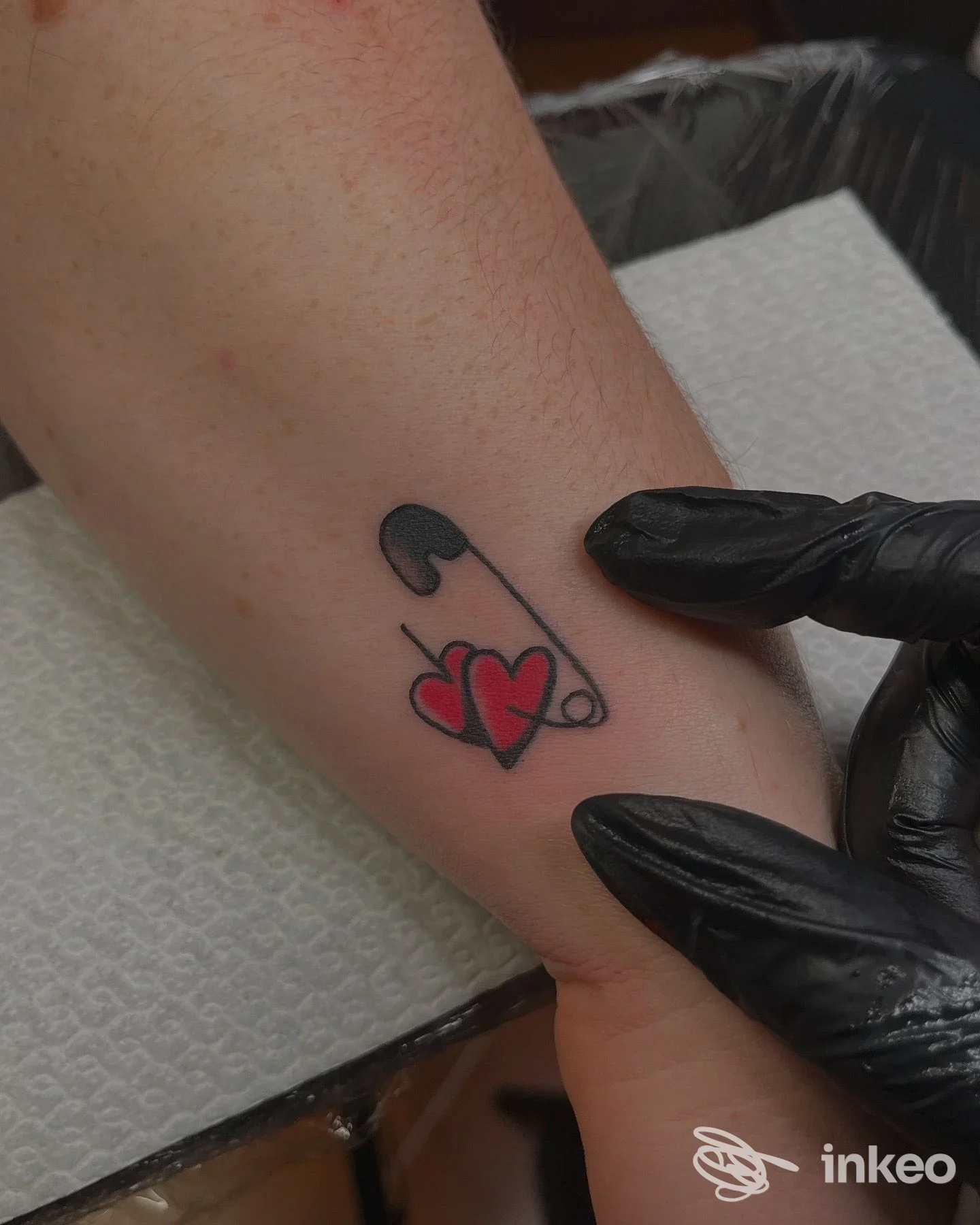 Tatuaggio su avambraccio con spilla stilizzata e due cuori rossi, foto scattata nello studio BOTTEGANERA tattoos and more a Bologna.