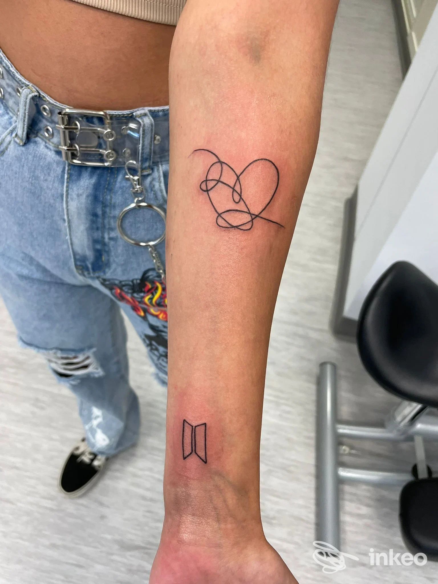 Avambraccio con due tatuaggi lineari neri: cuore stilizzato e piccolo simbolo geometrico; foto di Riff Raff Tattoo, Nola.