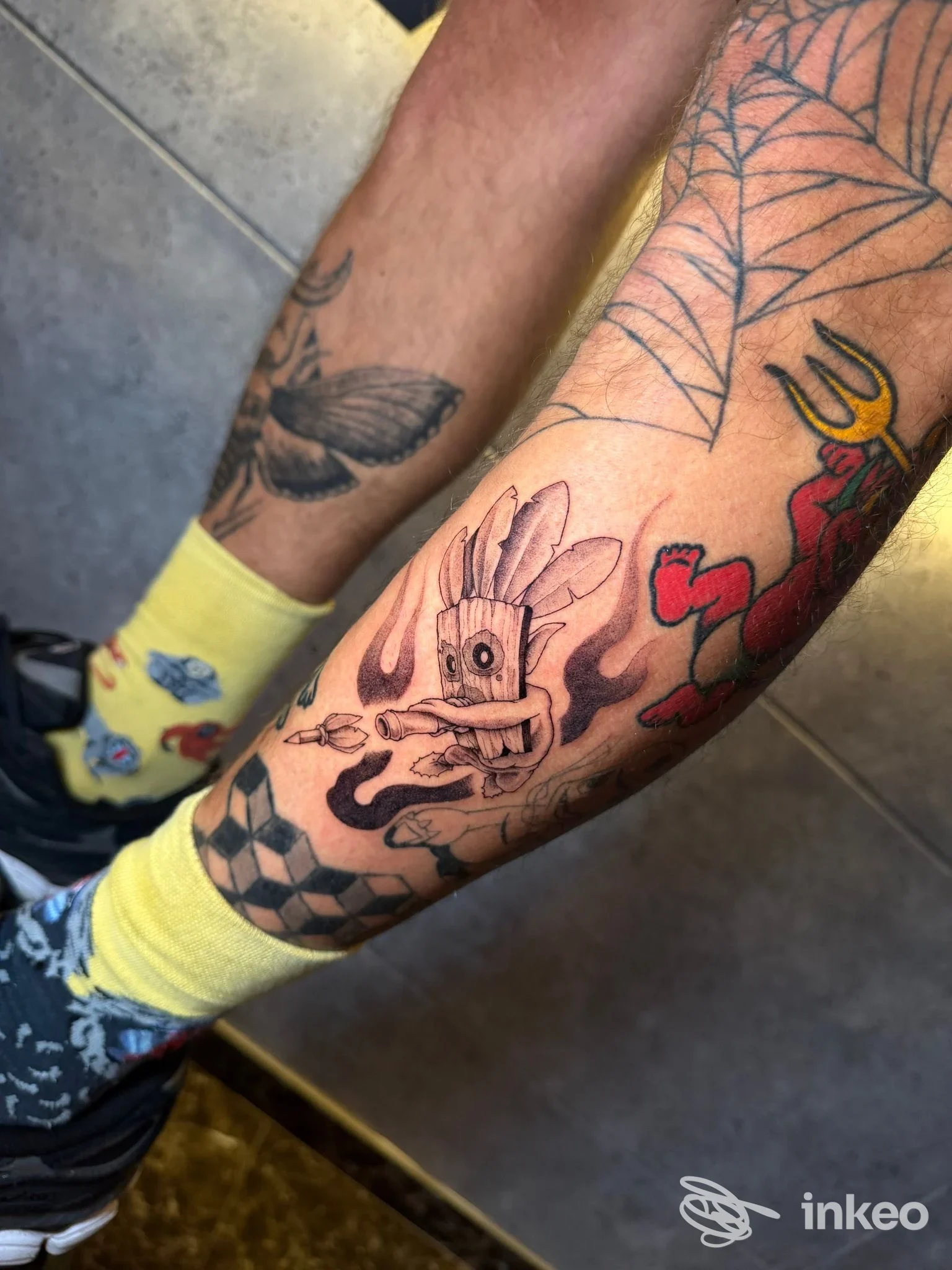 Dettaglio del polpaccio con tatuaggi realizzati da Artwork Studio Tattoo & PMU, Napoli: personaggio stilizzato, scacchi e motivi colorati sulla pelle.