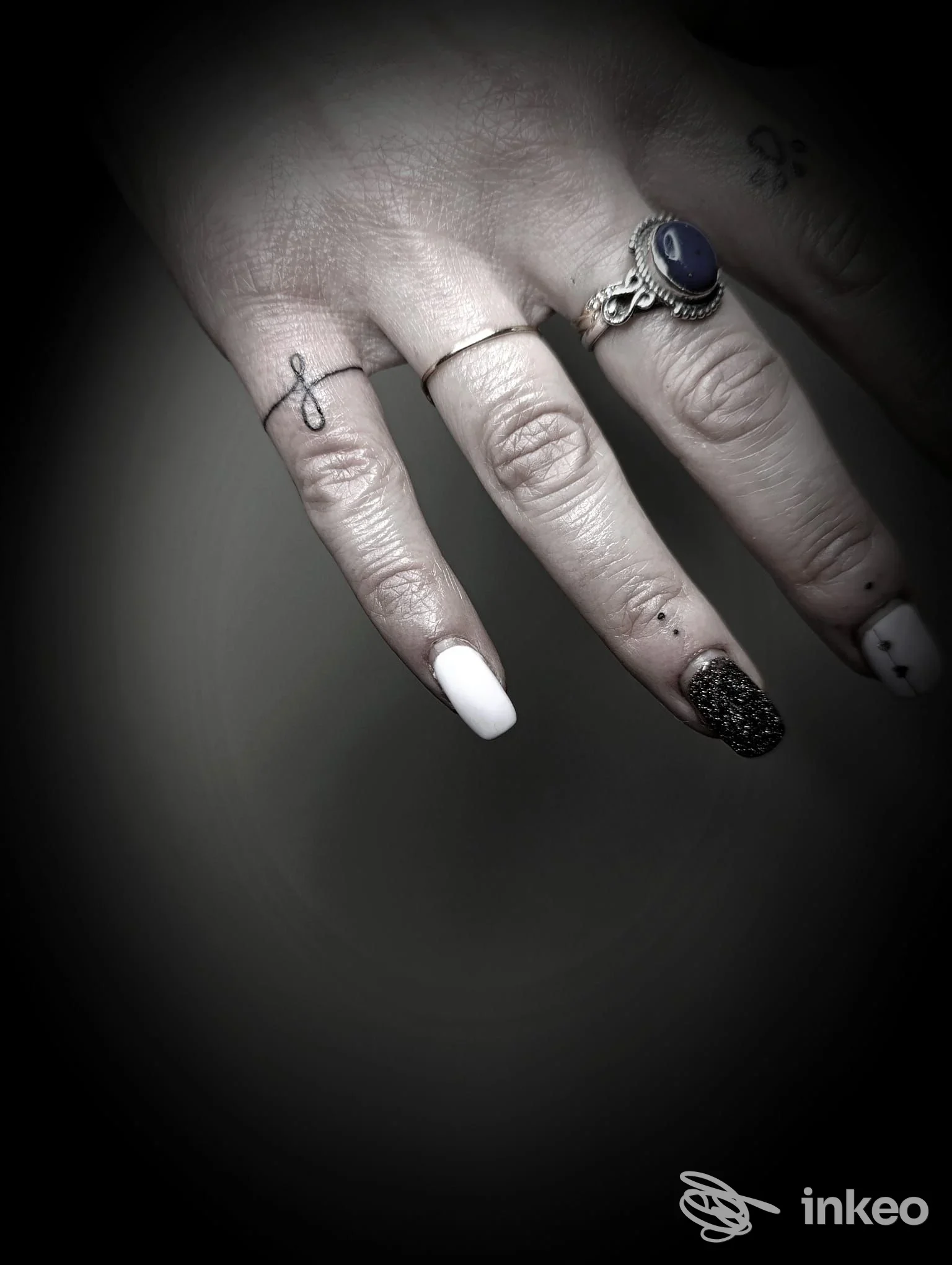 Mano fotografata con piccoli tatuaggi lineari sulle dita e anelli; immagine fornita dallo studio Inciso Tattoo Lab, Modena.