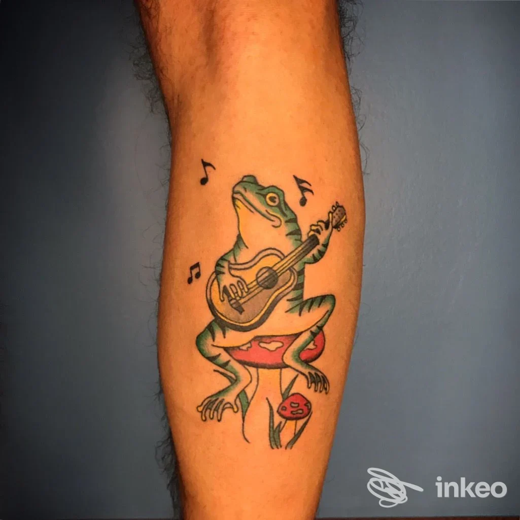 Tattoo colorato di una rana che suona una chitarra seduta su un fungo, sul polpaccio. Blue Tiger Tattoo shop, Forlì.