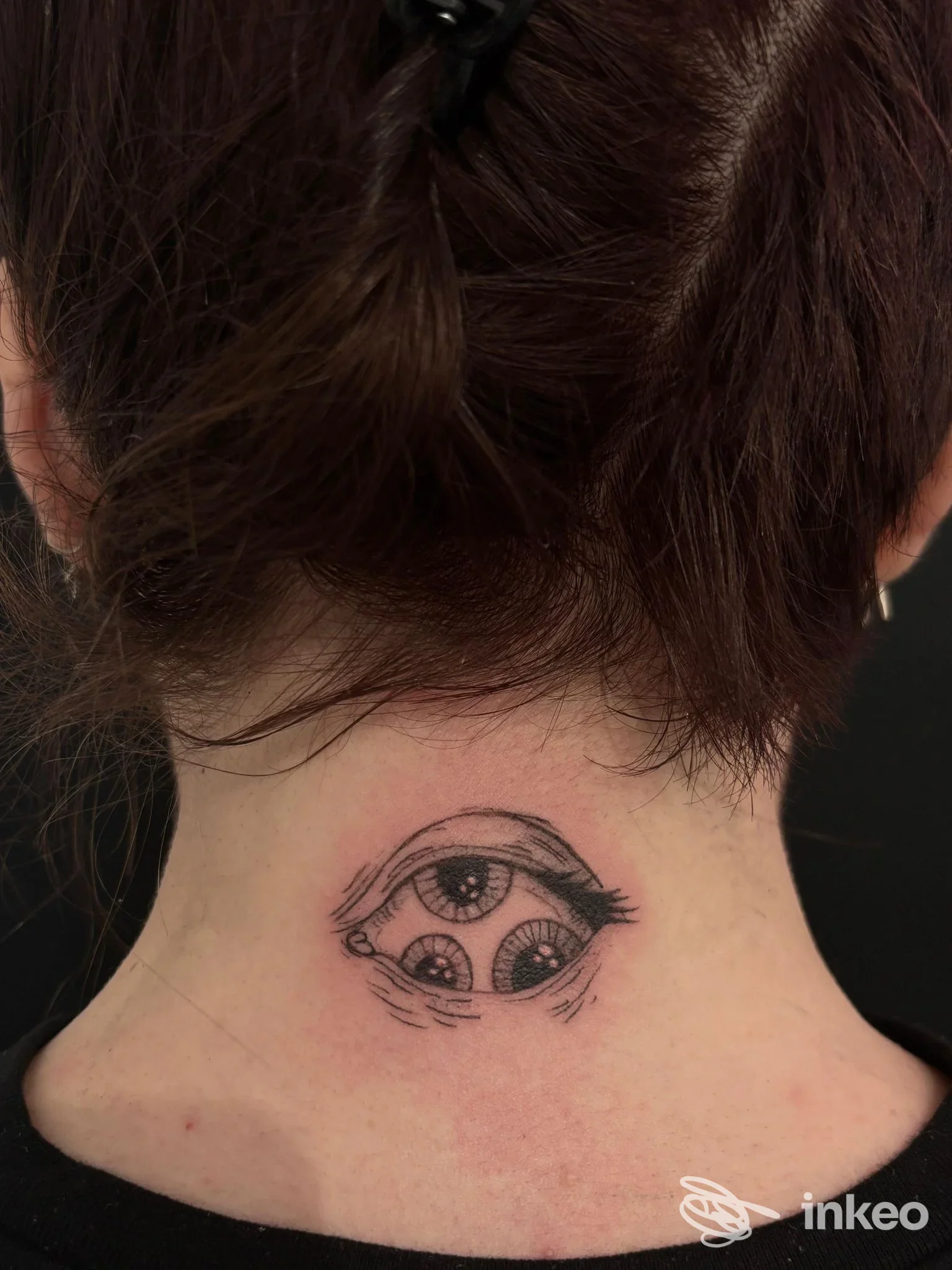 Tattoo sul retro del collo raffigurante un occhio con dettagli grafici, realizzato sulla pelle del soggetto in tinta nera su fondo chiaro.