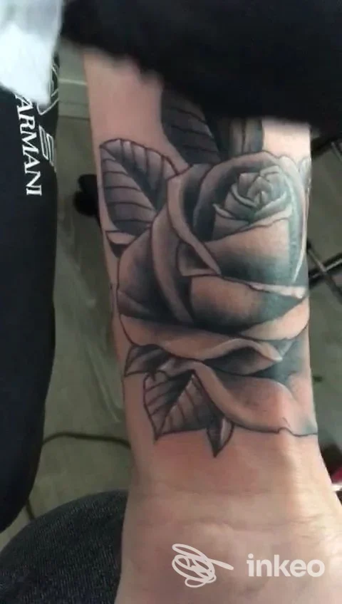 Tatuaggio realistico di rosa su avambraccio, in tonalità grigio/nera, visibile sulla pelle reale.