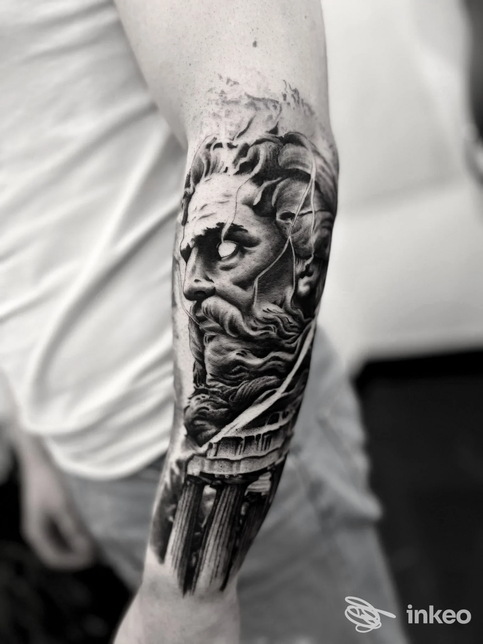 Tatuaggio realistico in bianco e nero su avambraccio, Tigano Tattoo Clinic ad Acate mostra un volto scultoreo e colonne.