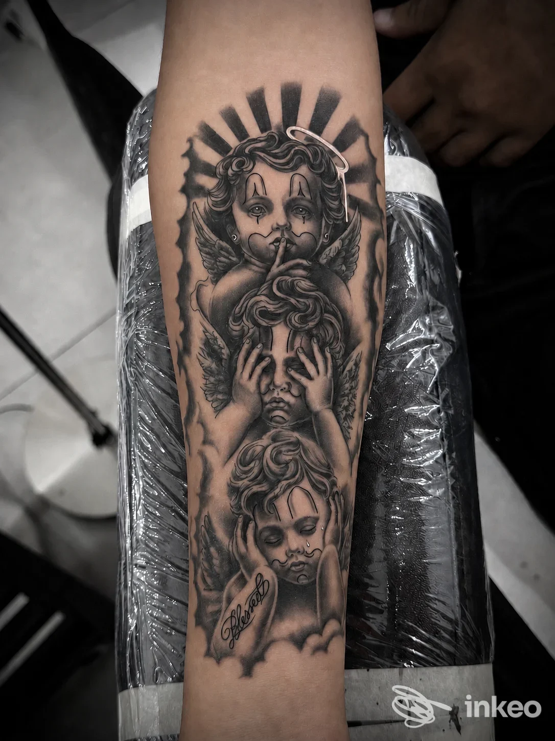 Tatuaggio realistico in bianco e nero con tre cherubini sull'avambraccio, foto fornita da Da Family Ink Tattoo Shop, Ispica.
