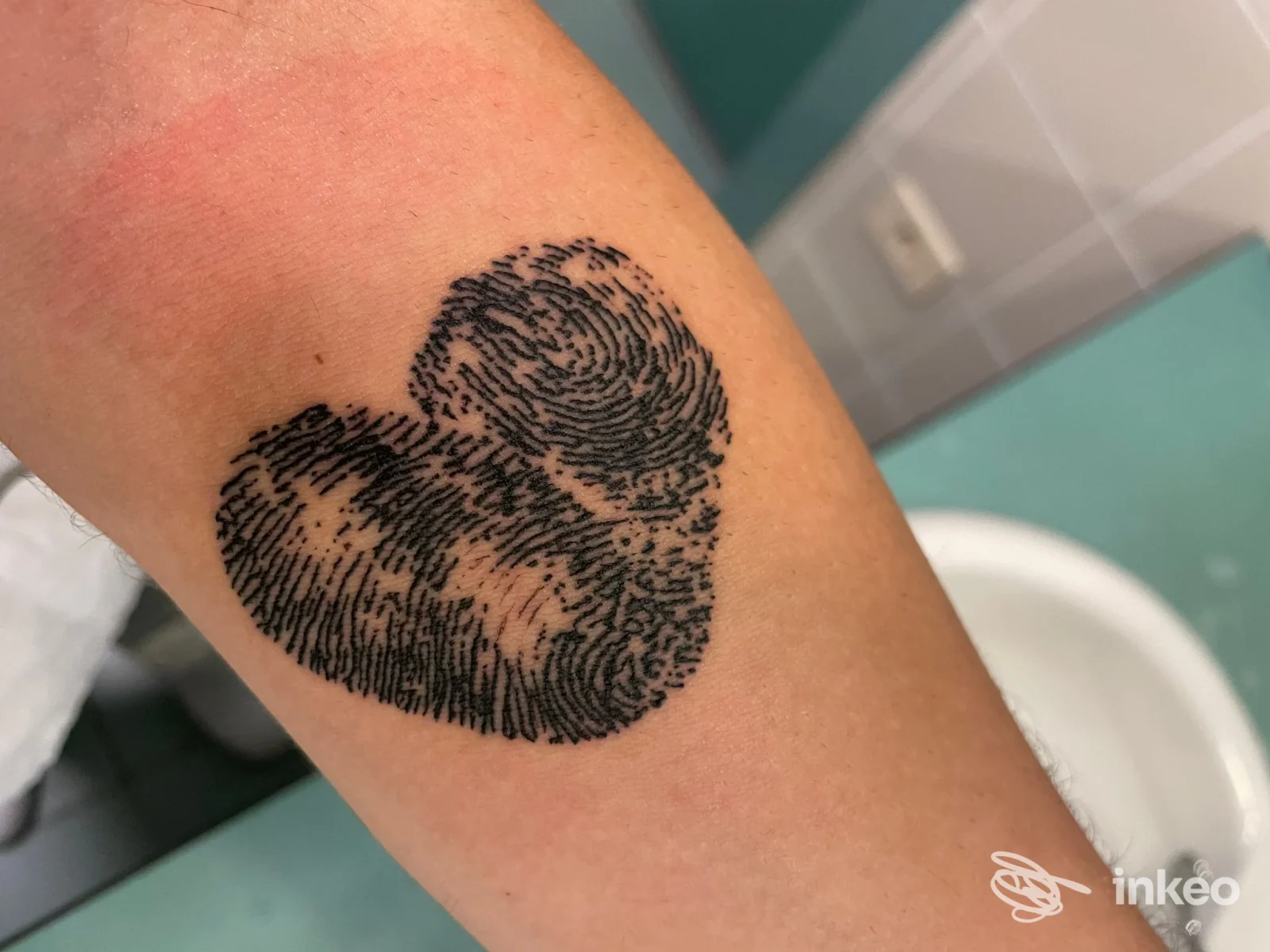 Tattoo a cuore con motivo a impronta digitale visibile sull’avambraccio, tatuaggio nero ben definito.