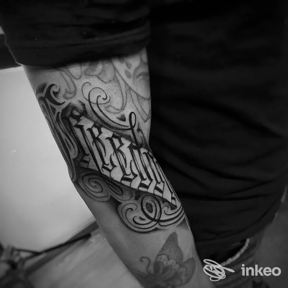 Primo piano di tatuaggio calligrafico e ornamentale sull'avambraccio, foto fornita da Swan Song Tattoo, Capoliveri.