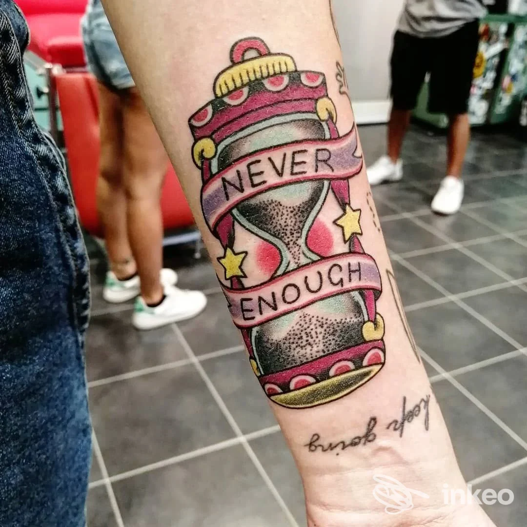 Avambraccio con tatuaggio a clessidra colorata e nastro con scritta "NEVER ENOUGH", immagine fornita da Tatuaggi da Claudio a Follonica.