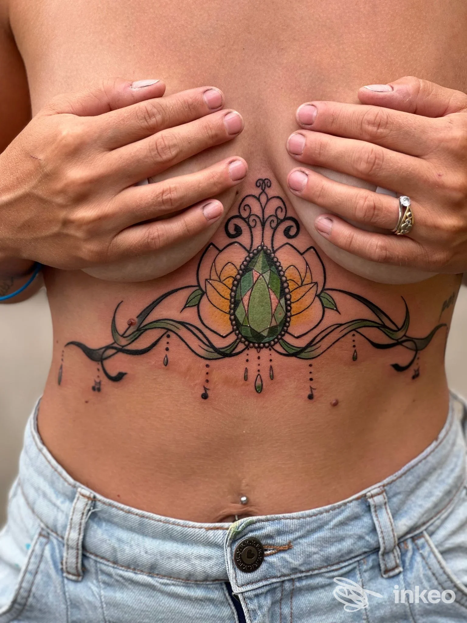 Tatuaggio ornamentale sotto il petto con gemma verde, realizzato da Chibi Moon Studio Tattoo a Torre Pellice.