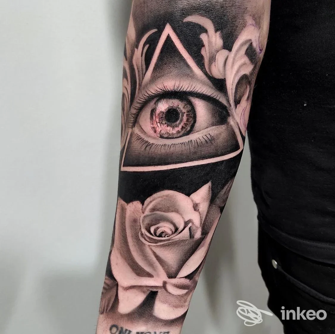 Tatuaggio su avambraccio raffigurante occhio incorniciato da triangolo e rosa, realizzato in toni neri e grigi.