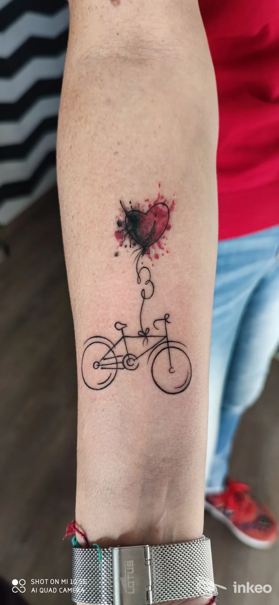 Tatuaggio su avambraccio con bicicletta stilizzata in linework e cuore acquerellato sopra, foto da Elder Sign Tattoo, Massa Marittima.