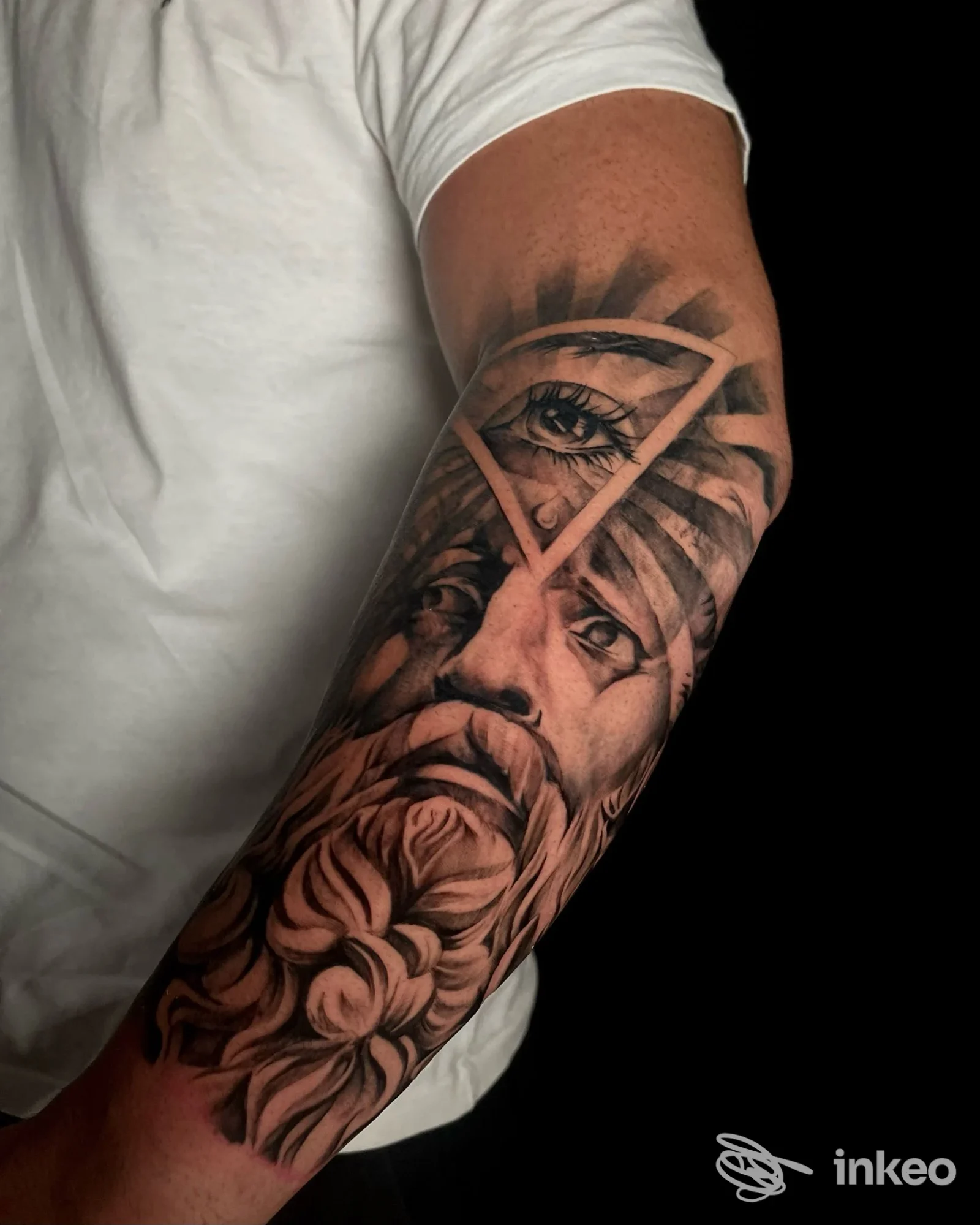 Tatuaggio realistico black & grey su avambraccio con volto stilizzato e occhio triangolare. Madness Tattoo, San Giorgio delle Pertiche.
