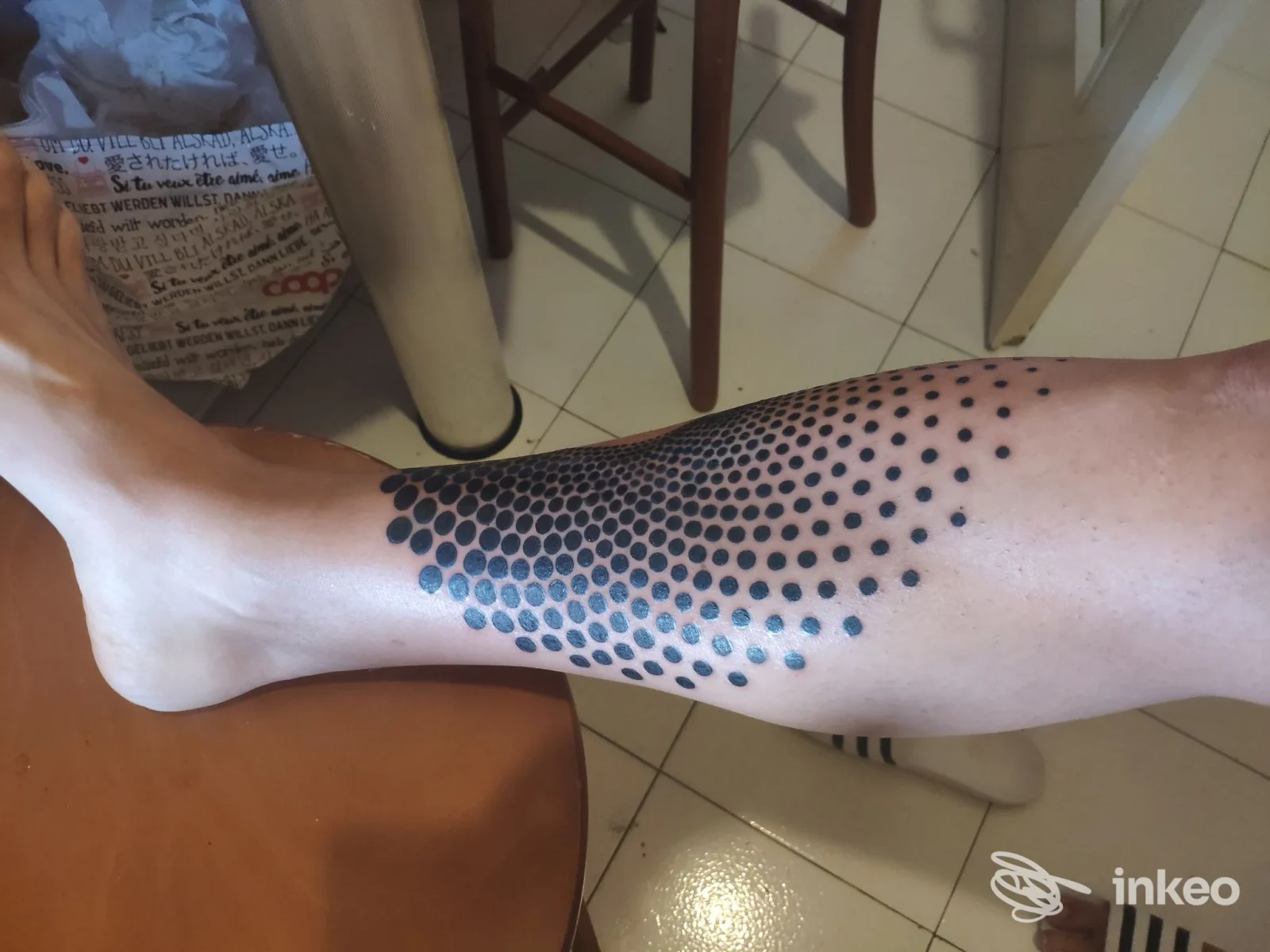 Tattoo a puntini blu scuro lungo l’avambraccio/gamba, visibile su pelle umana, scatto dall’alto.