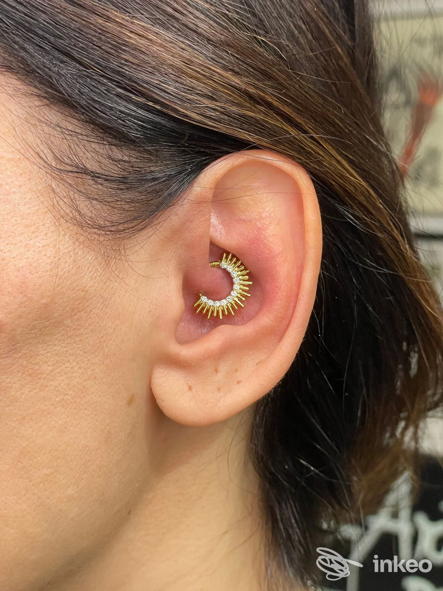 Primo piano di un piercing alla conca con gioiello dorato, immagine inviata da Hell's piercings a Piossasco.