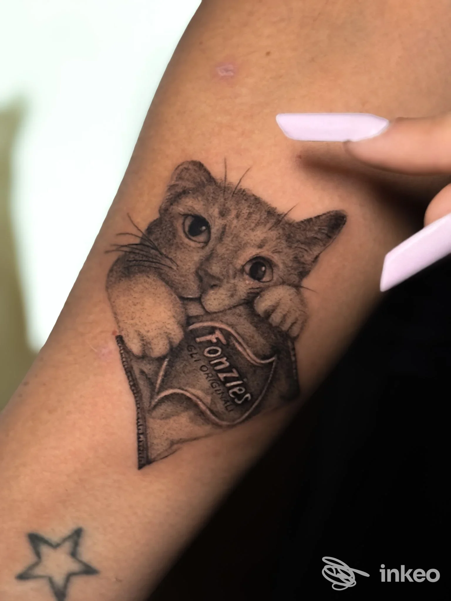Tattoo sul braccio raffigurante un gattino che tiene un cuore con scritta, eseguito sulla pelle.